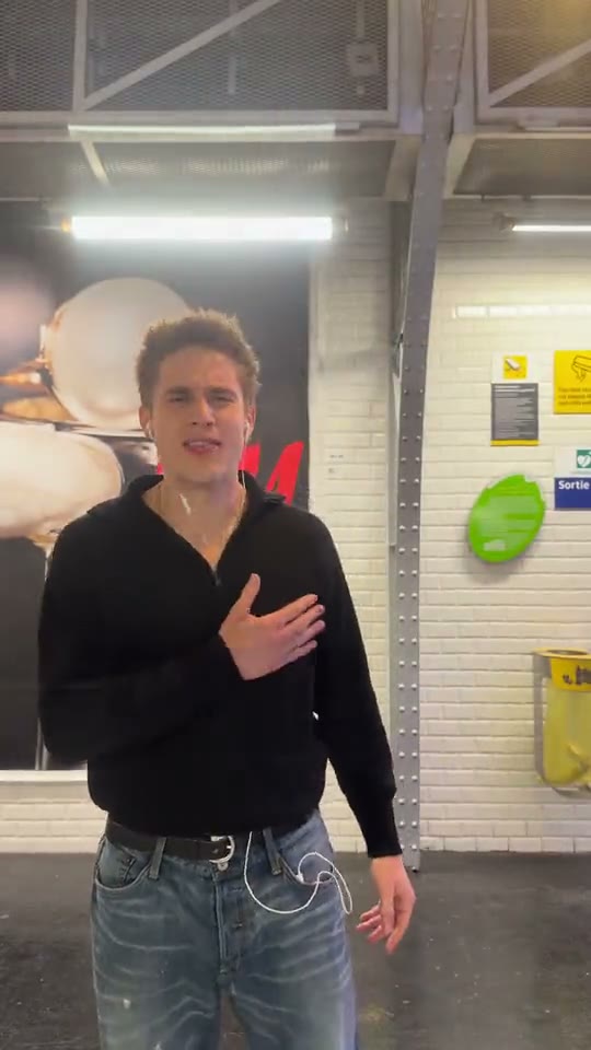 El protagonista de frente, con las manos ante el pecho y publicidad en el andén